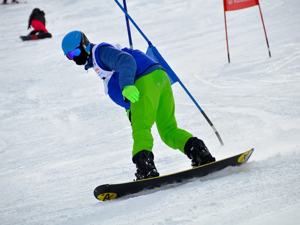 Snowboarder in grüner Hose fährt an einem roten Tor vorbei.